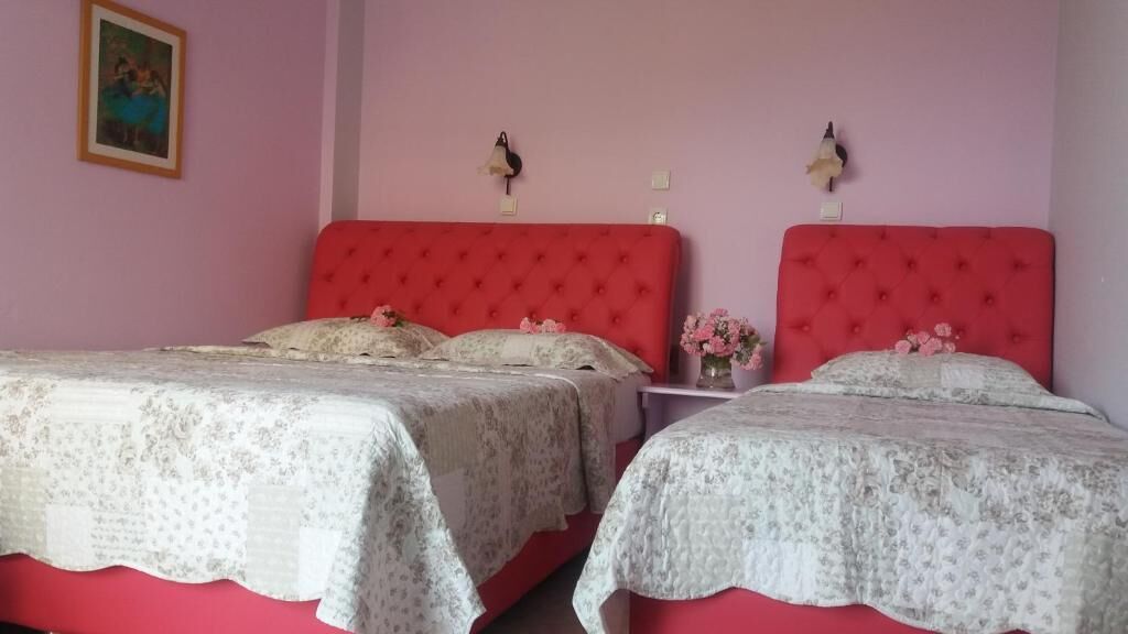Een slaapkamer met twee bedden, elk met een rode hoofdbord en een wit bloemenbedekking. Daartussen staat een nachtkastje met een bloevas.