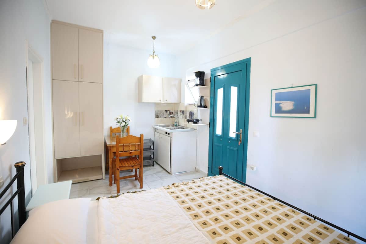 A bedroom with a bed, a desk, a chair, a kitchenette, and a bathroom.
