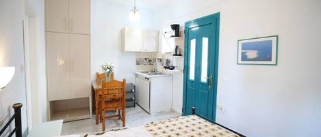 Un dormitorio con cama, escritorio, silla, kitchenette y baño.