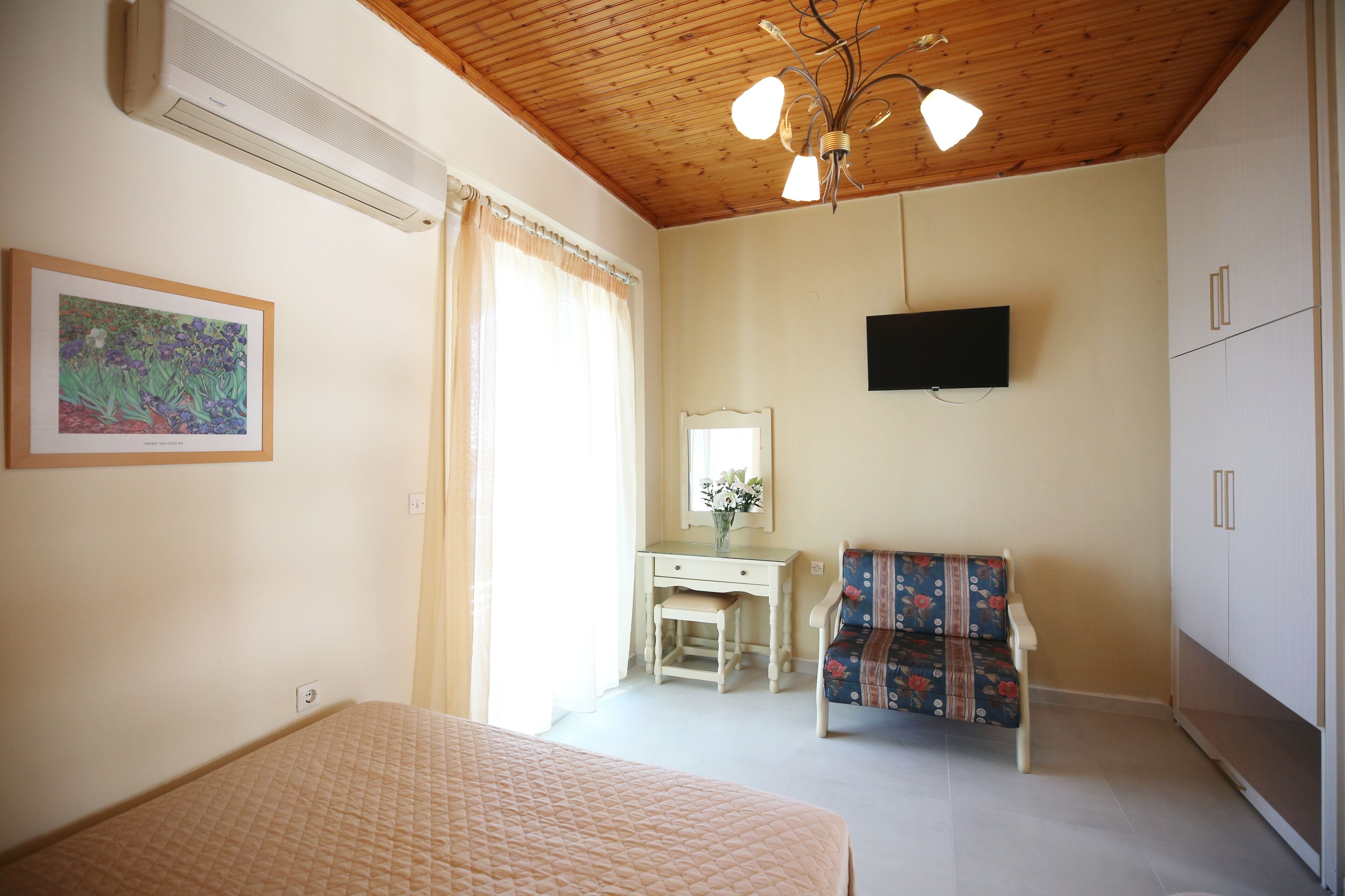 Un dormitorio con cama, escritorio, silla, televisor y ventana con cortinas.