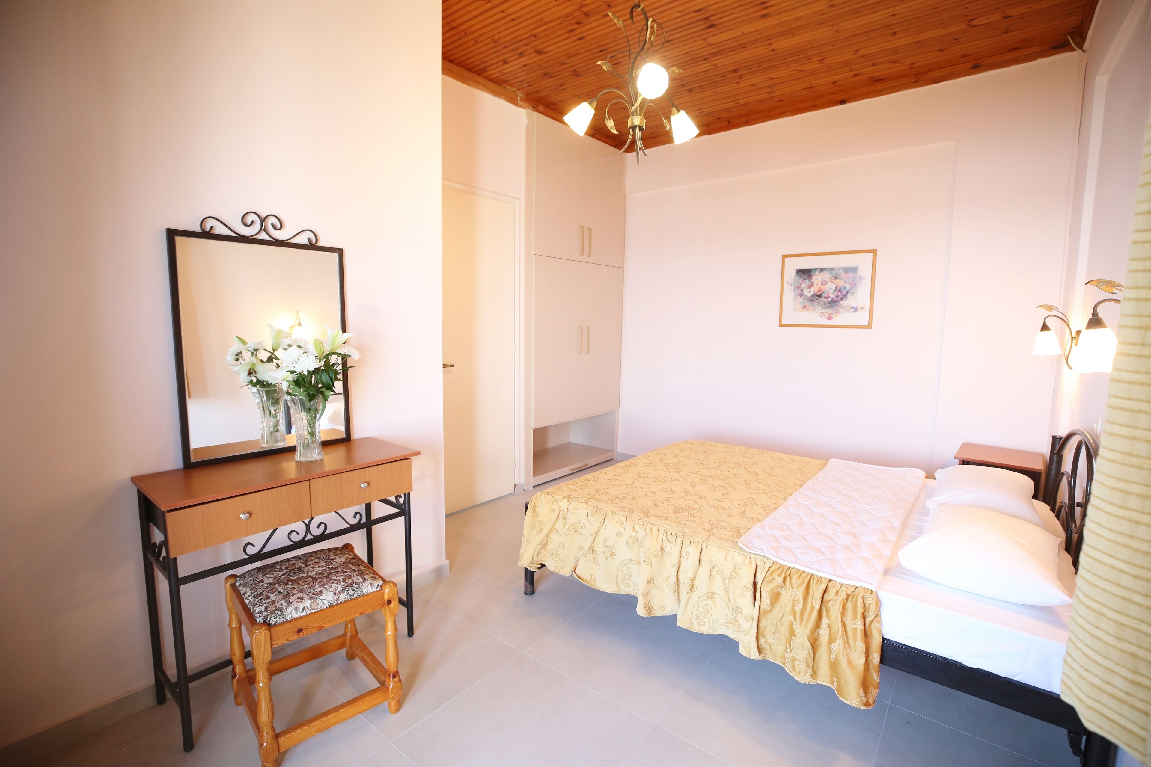 A bedroom with a bed, a wooden dresser, a mirror, and a small stool.