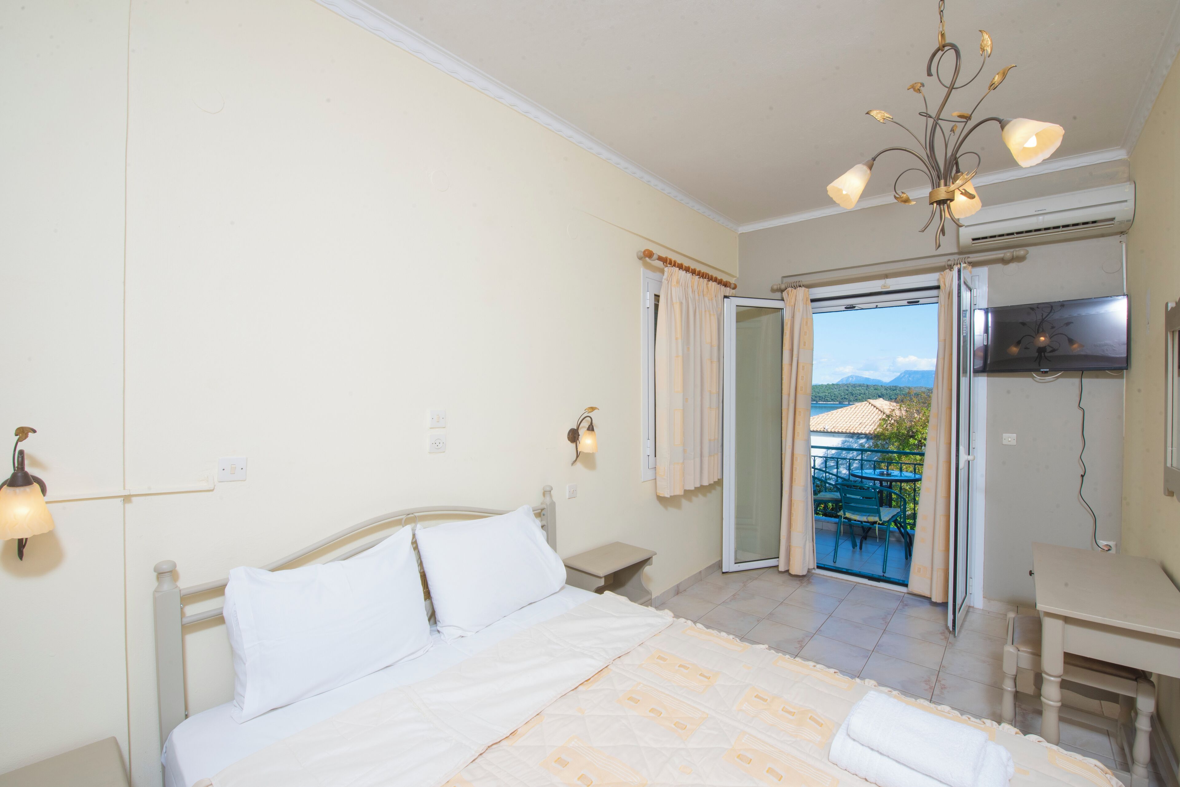 A bedroom with a bed, a desk, and a balcony with a view.