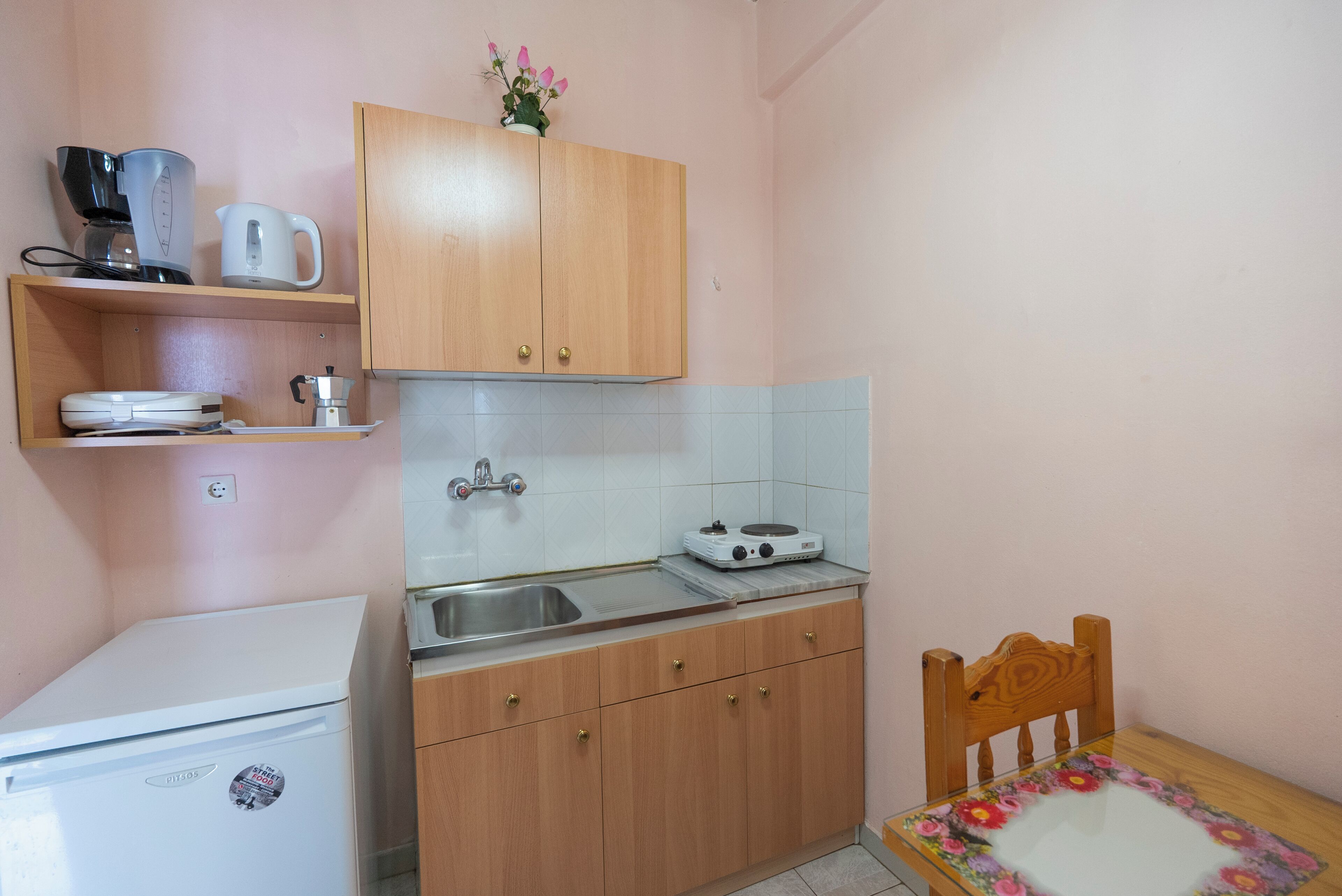 A compact kitchen with a refrigerator, a coffee maker, a kettle, a stove, and a sink.