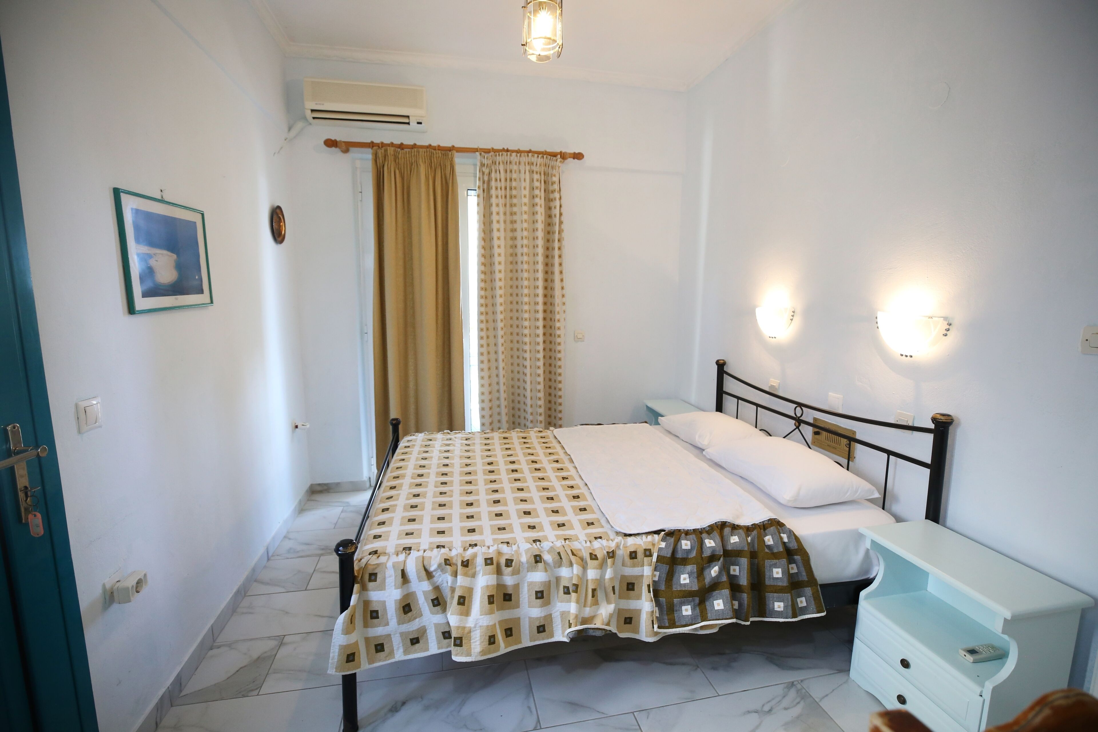 A bedroom with a bed, a nightstand, a wall-mounted light, and a window with curtains.