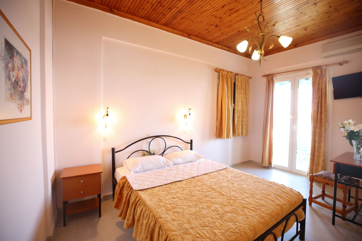 A bedroom with a bed, bedside tables, a desk, a chair, a TV, and a window with curtains.