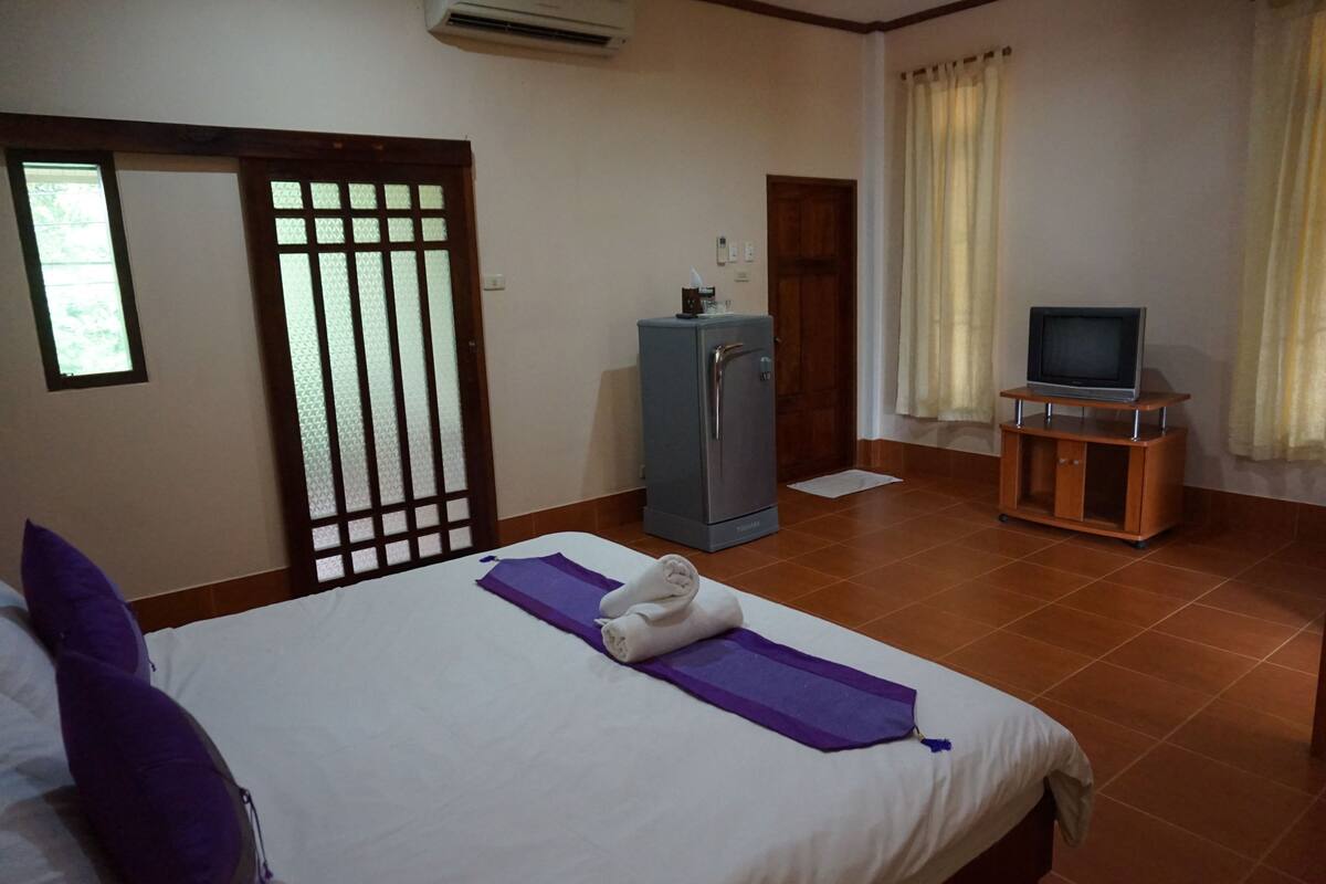 A hotel room with a bed, a small cabinet, a television on a stand, and a window with curtains.