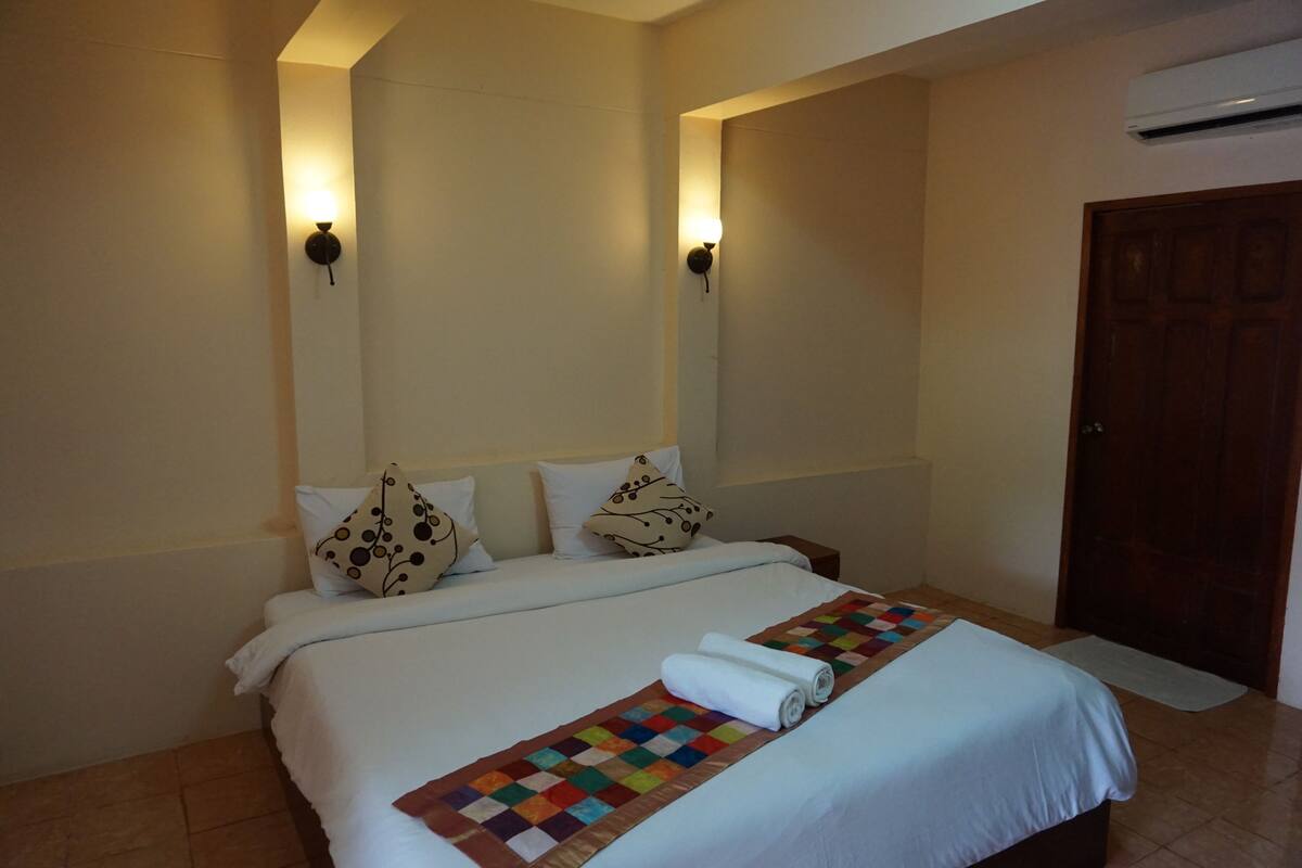 A neatly made bed with a colorful quilt, two wall-mounted lights, and a wooden door.