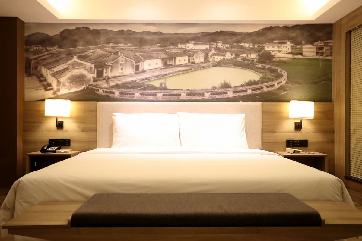 Hotelkamer met een groot bed, twee bedlampjes, een nachtkastje met een telefoon, en een muurschildering van een stadsbeeld.