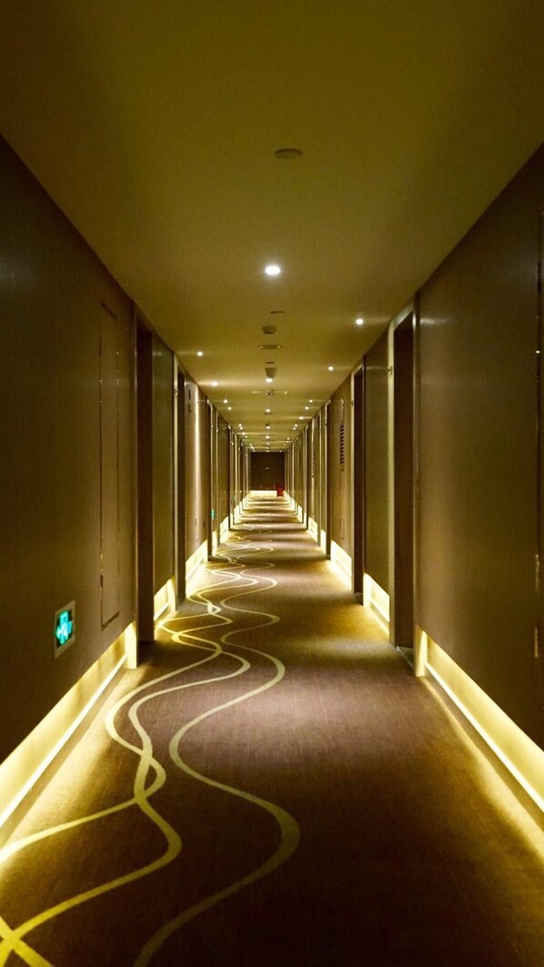 Un largo y estrecho pasillo de hotel con alfombra estampada e iluminación empotrada.