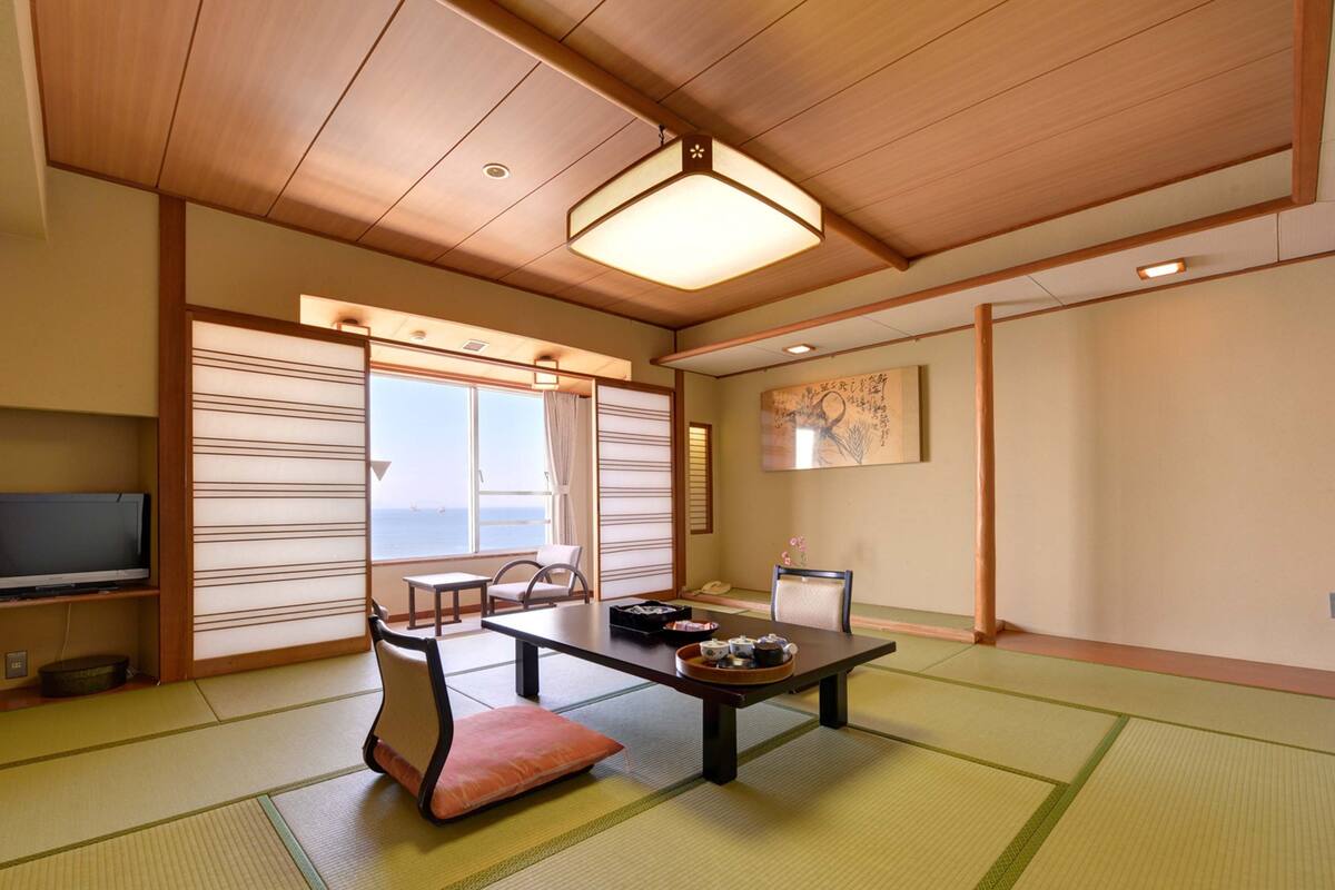 A traditional Japanese room with tatami flooring, a low table with tea set, and a view of the sea through shoji screens.