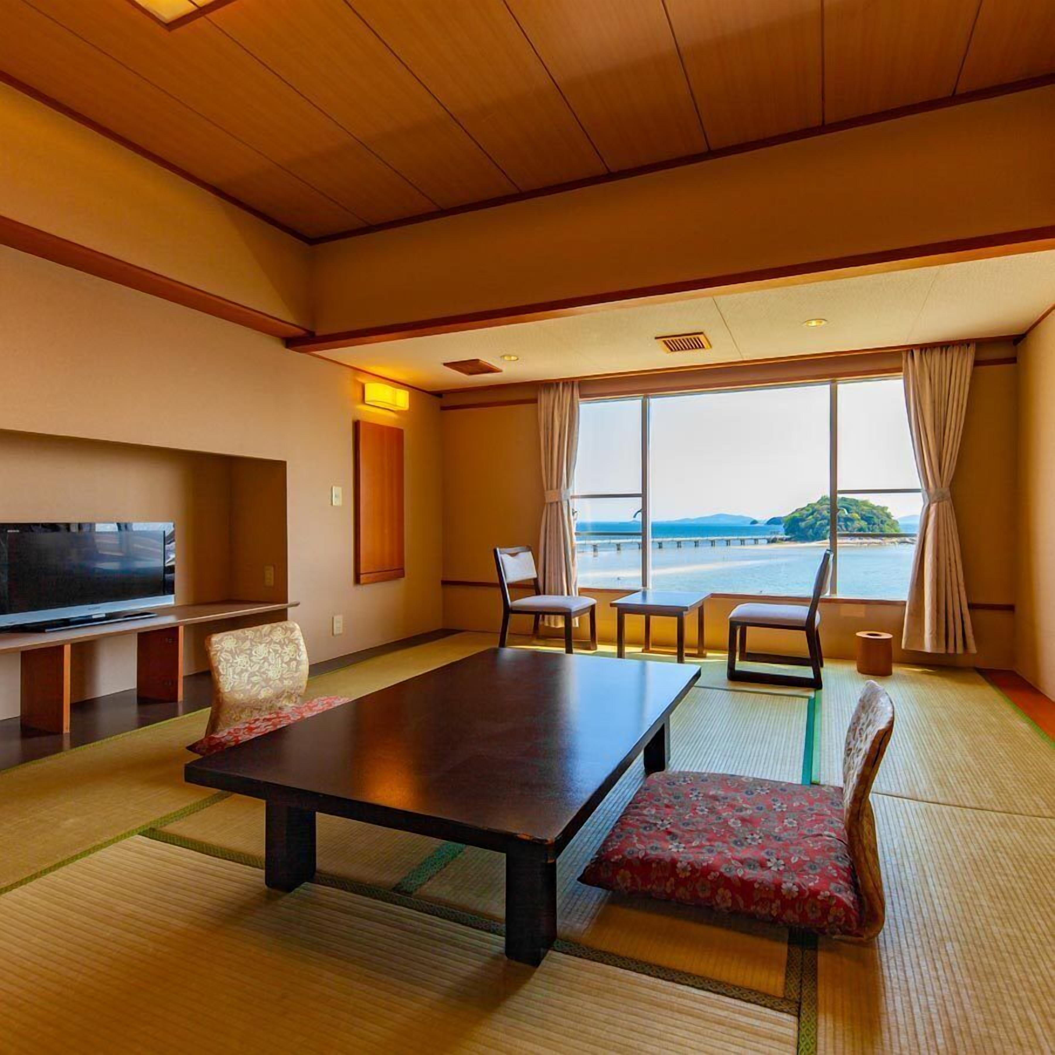 A room with a large window, a television, a table, and chairs.