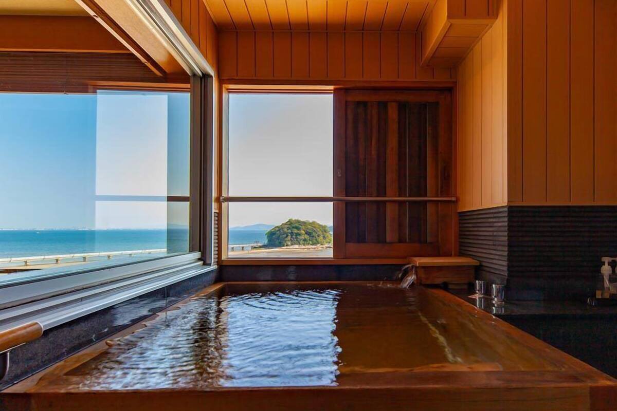 A wooden interior with a large window offering a view of the sea and a distant island.