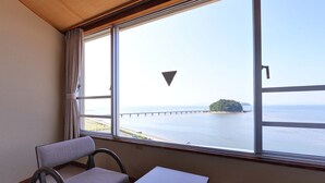 A room with a large window offering a view of a bridge and an island. There is a small table and two chairs. - Hotel Takeshima (Gamagori)