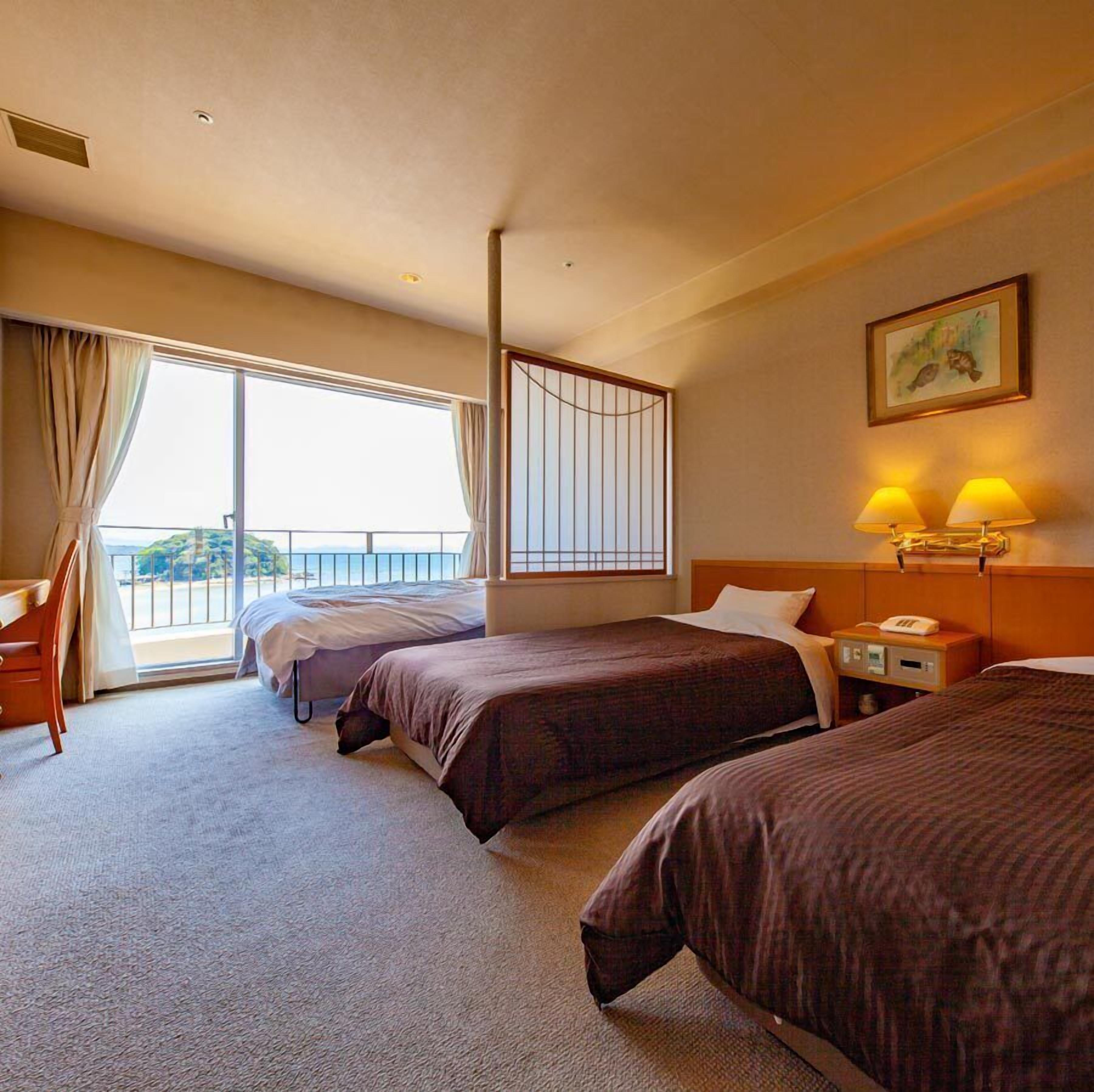 A hotel room with two beds, a desk, a chair, a window with curtains, a painting, and a nightstand with lamps.