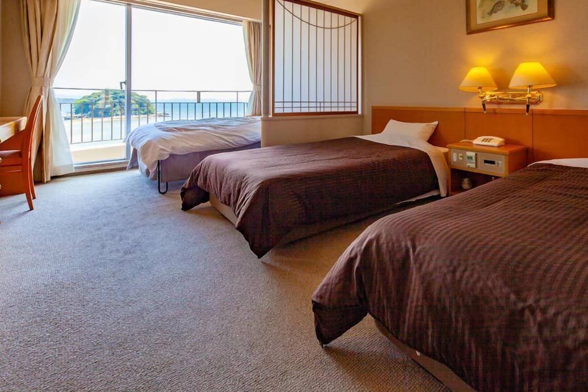 A hotel room with two beds, a desk, a chair, a window with curtains, a painting, and a nightstand with lamps.