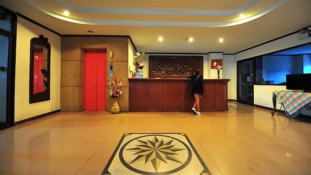 A hotel lobby with a reception desk, a red door, a large decorative wall, and a patterned floor design. - B.P Grand Service Apartment (Chiang Mai)