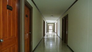 A long, narrow hallway with wooden doors on one side and a tiled floor. - B.P Grand Service Apartment (Chiang Mai)
