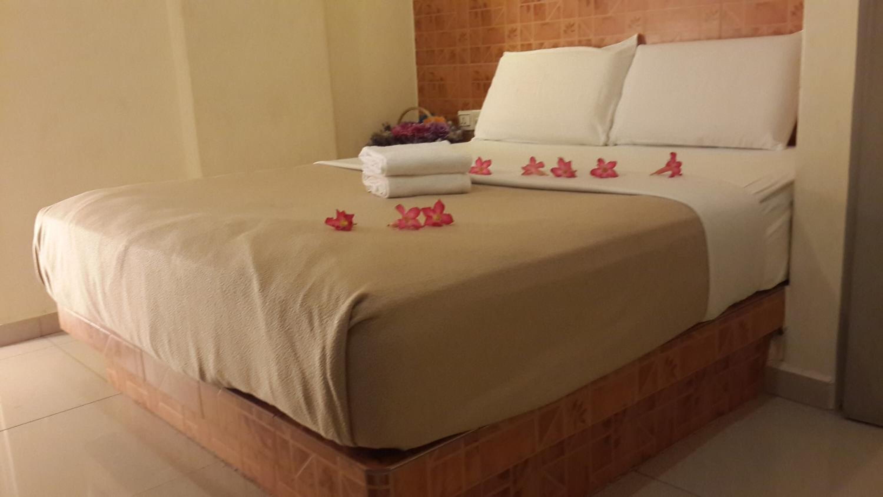 A neatly made bed with a beige bedspread, white pillows, and pink flowers on the bed.
