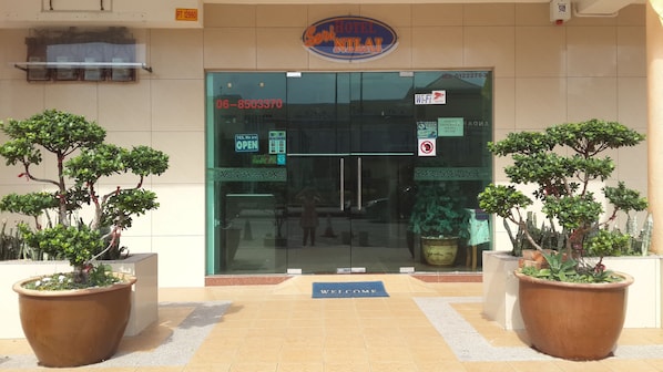 La entrada de un hotel con una puerta de cristal, un letrero que dice 'Sí, estamos ABIERTOS' y un felpudo que dice 'BIENVENIDOS'.