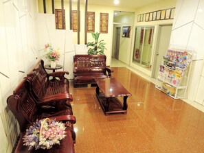 Una zona de recepción con bancos de madera, una pequeña mesa con un jarrón de flores y un mueble para revistas.