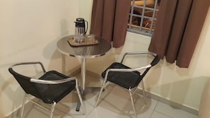 Una habitación pequeña con una mesa redonda y dos sillas negras. Hay una cafetera sobre la mesa.