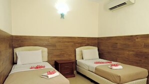 Ein Hotelzimmer mit zwei Betten, jedes mit einer beigen Tagesdecke, weißen Kissen und einem kleinen Nachttisch mit Schublade.