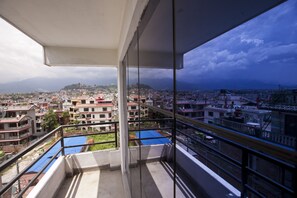 Un balcon offrant une vue sur le paysage urbain, avec des bâtiments et une chaîne de montagnes lointaine.