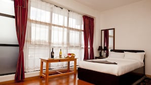 A bedroom with a bed, a wooden nightstand, a table with a bottle and fruit, and a window with curtains. - The Boudha Inn (Kathmandu)