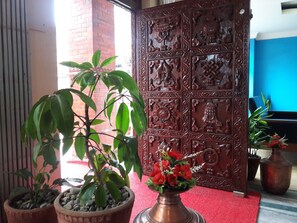 Una planta en maceta con flores rojas, una puerta decorativa con tallas intrincadas y una alfombra roja.