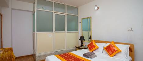 A hotel room with a bed, a wooden chair, a wardrobe, and a mirror.
