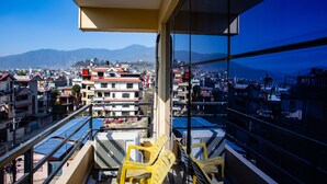 A balcony with yellow chairs, a view of a cityscape, and mountains in the distance. - The Boudha Inn (Kathmandu)