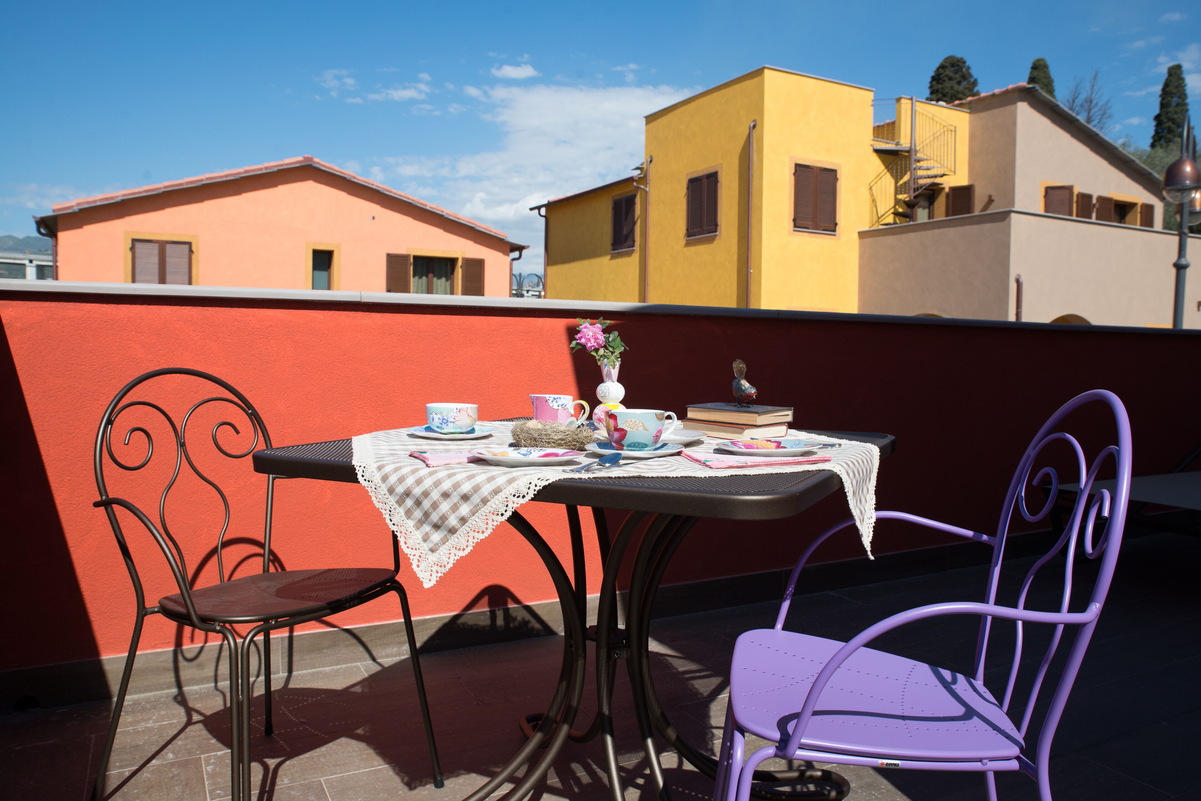 Ein Tisch mit Stühlen auf einer Terrasse, im Hintergrund Gebäude.