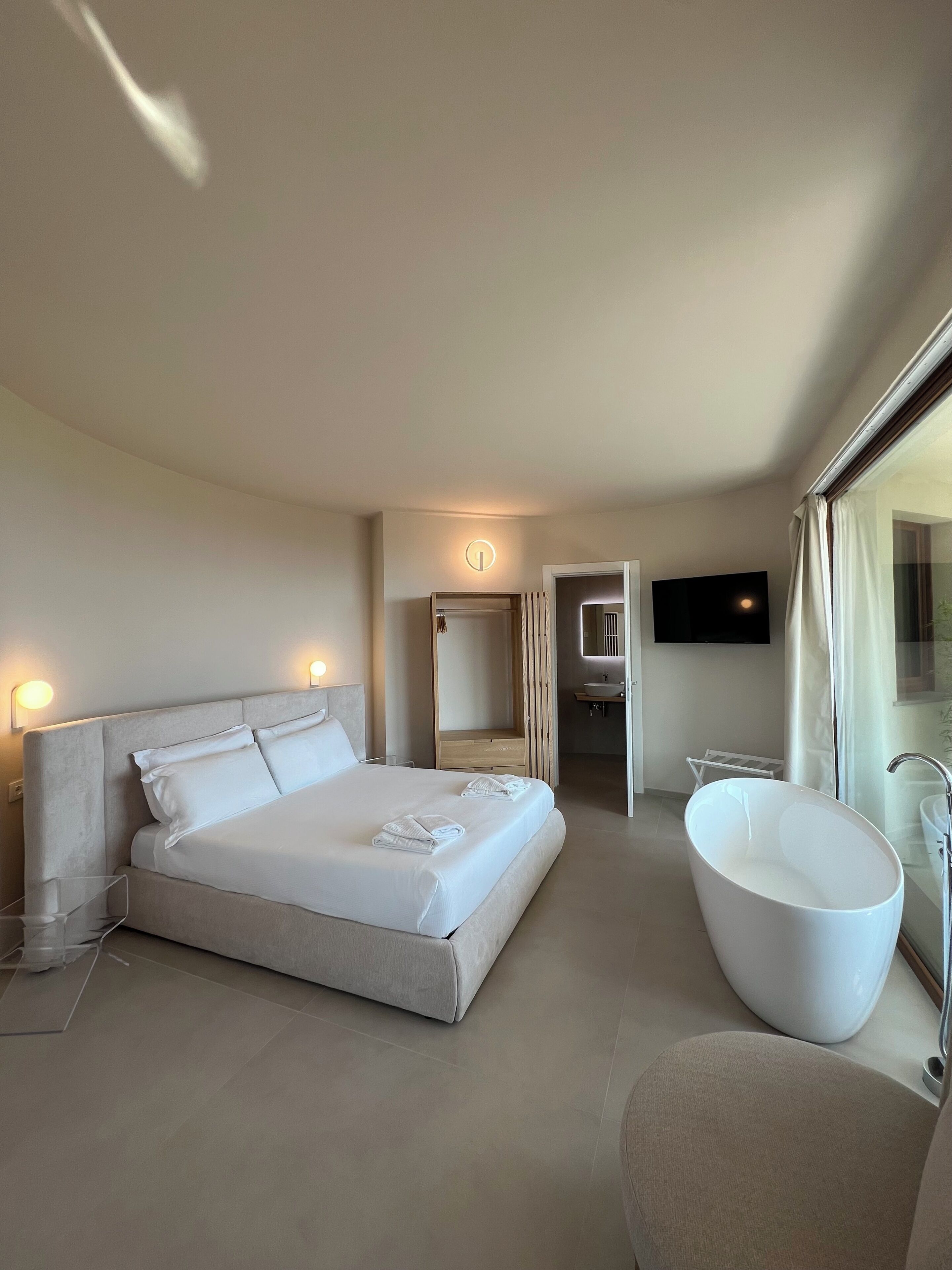 A modern hotel room with a large bed, a bathtub, and a TV mounted on the wall.