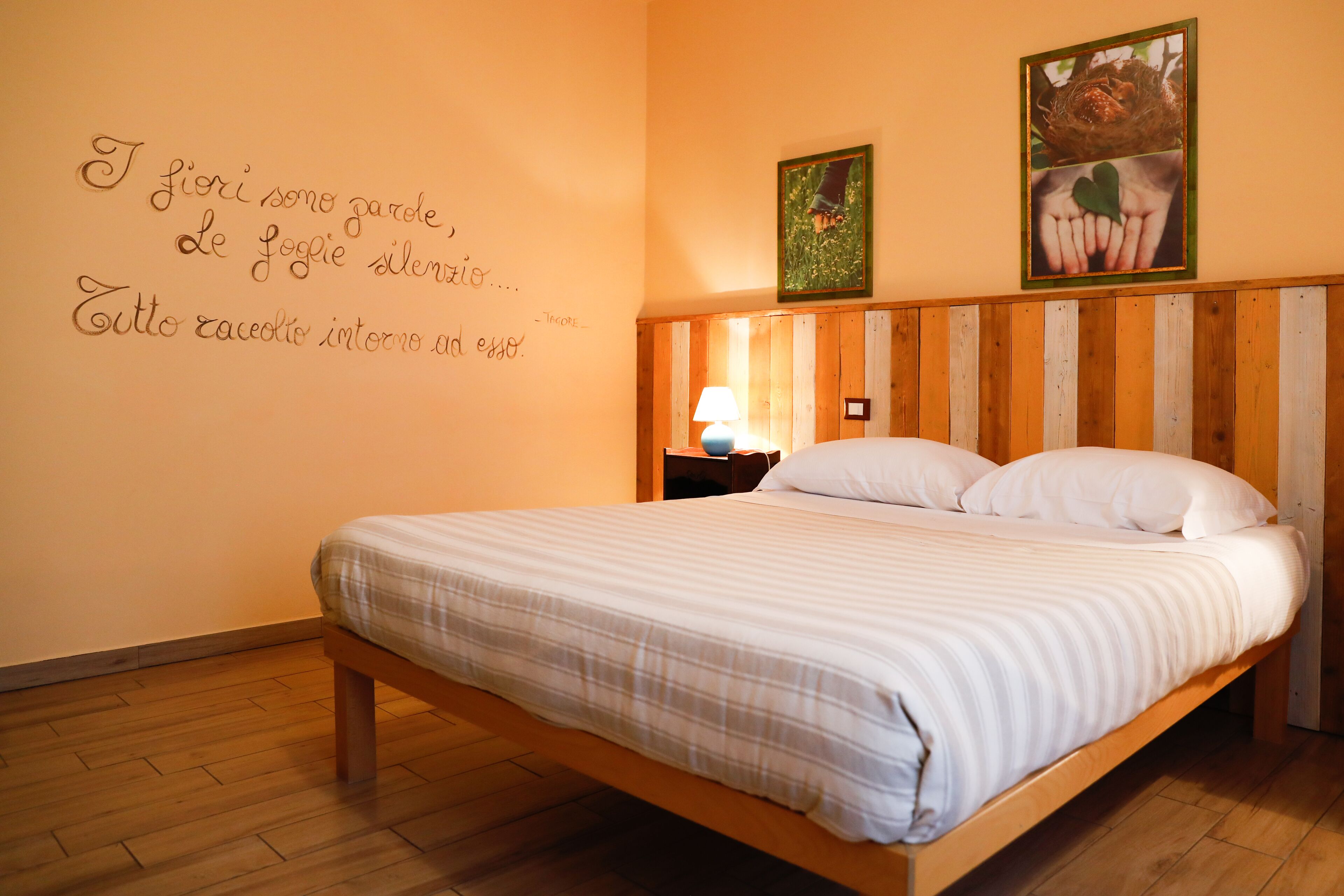 A bedroom with a wooden bed, a nightstand, a lamp, and two framed pictures on the wall.
