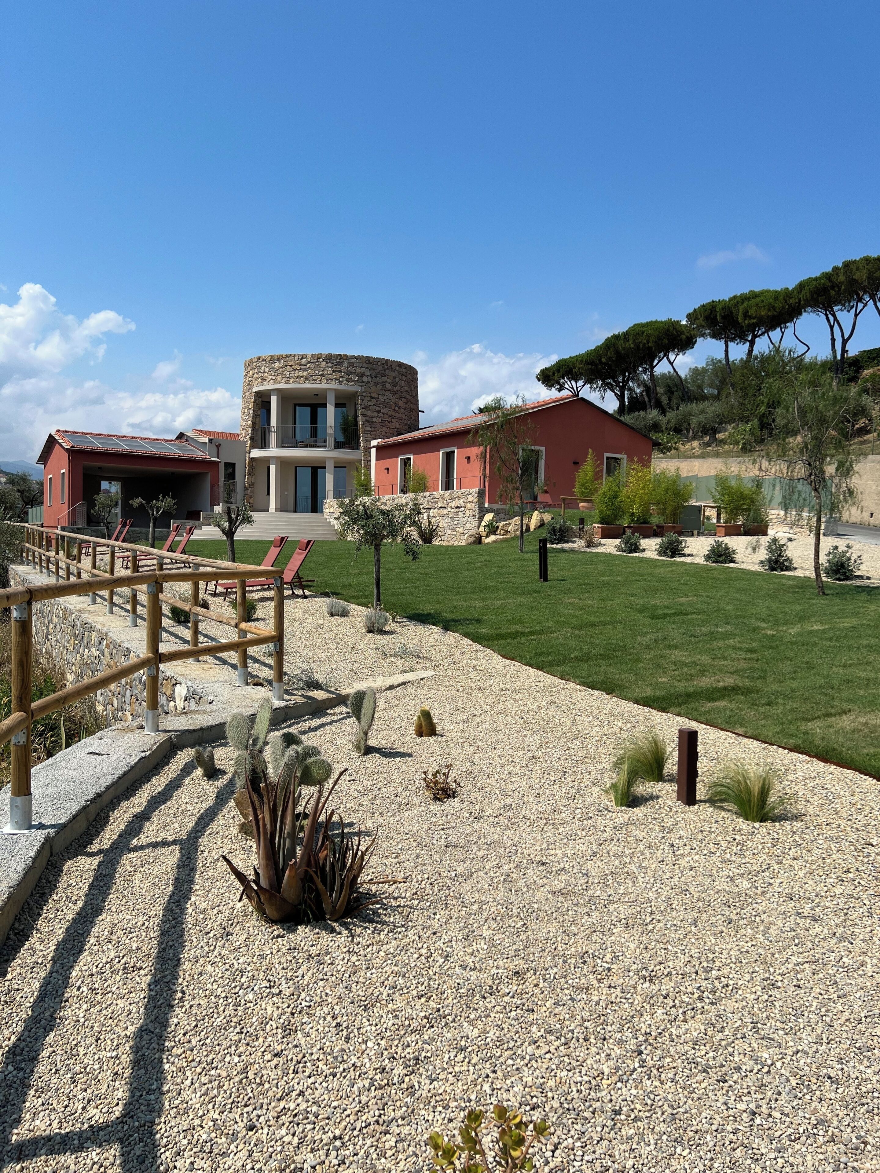 A modern building with a stone facade, a red-roofed structure, and a well-maintained lawn with cacti and shrubs.