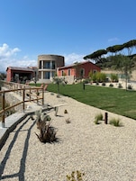 A modern building with a stone facade, a red-roofed structure, and a well-maintained lawn with cacti and shrubs.