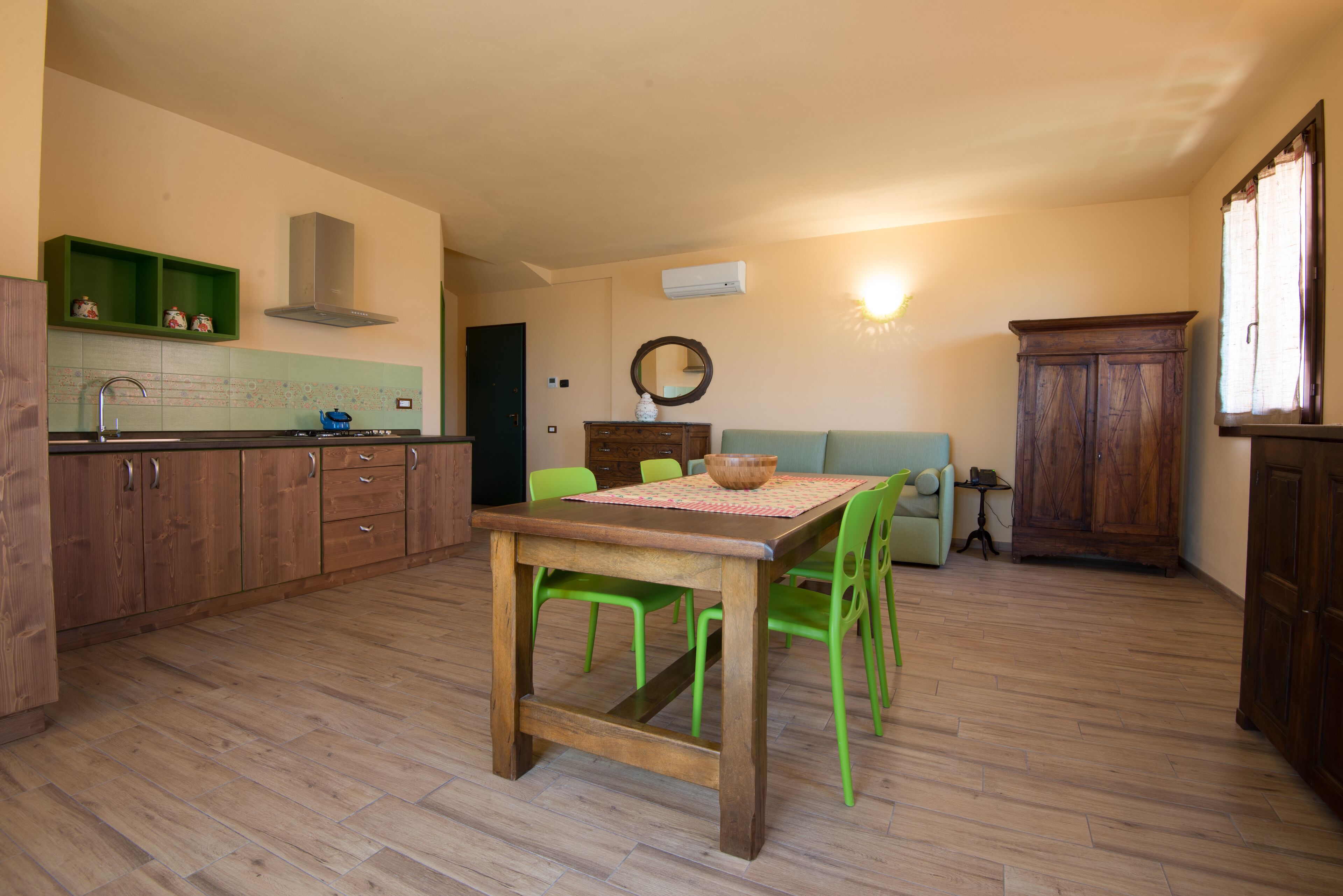 Une cuisine avec des meubles de rangement en bois, une table à manger avec des chaises et un canapé vert.