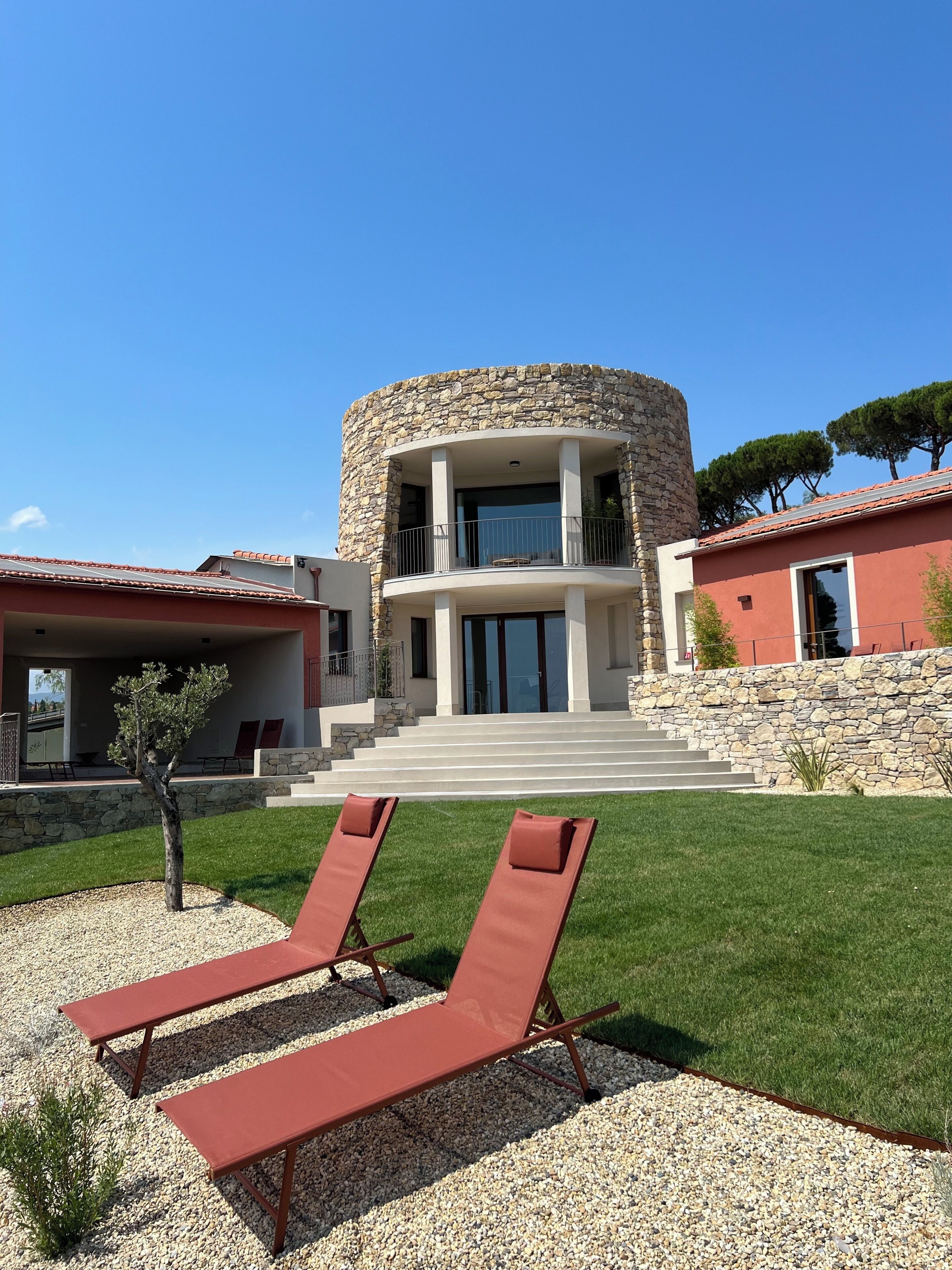 A modern house with a stone exterior, a balcony, and a well-maintained lawn with two lounge chairs.