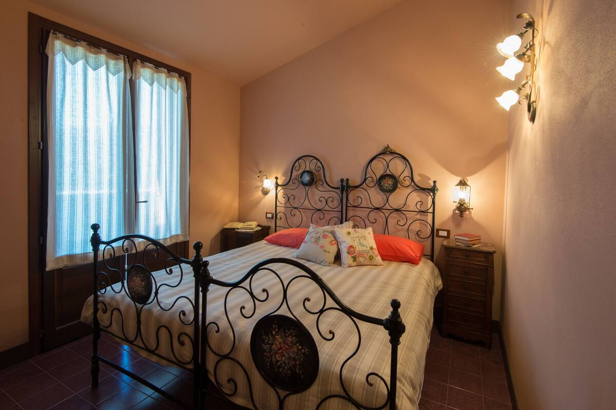 Un dormitorio con cama, cortinas, mesita de noche e iluminación en la pared.