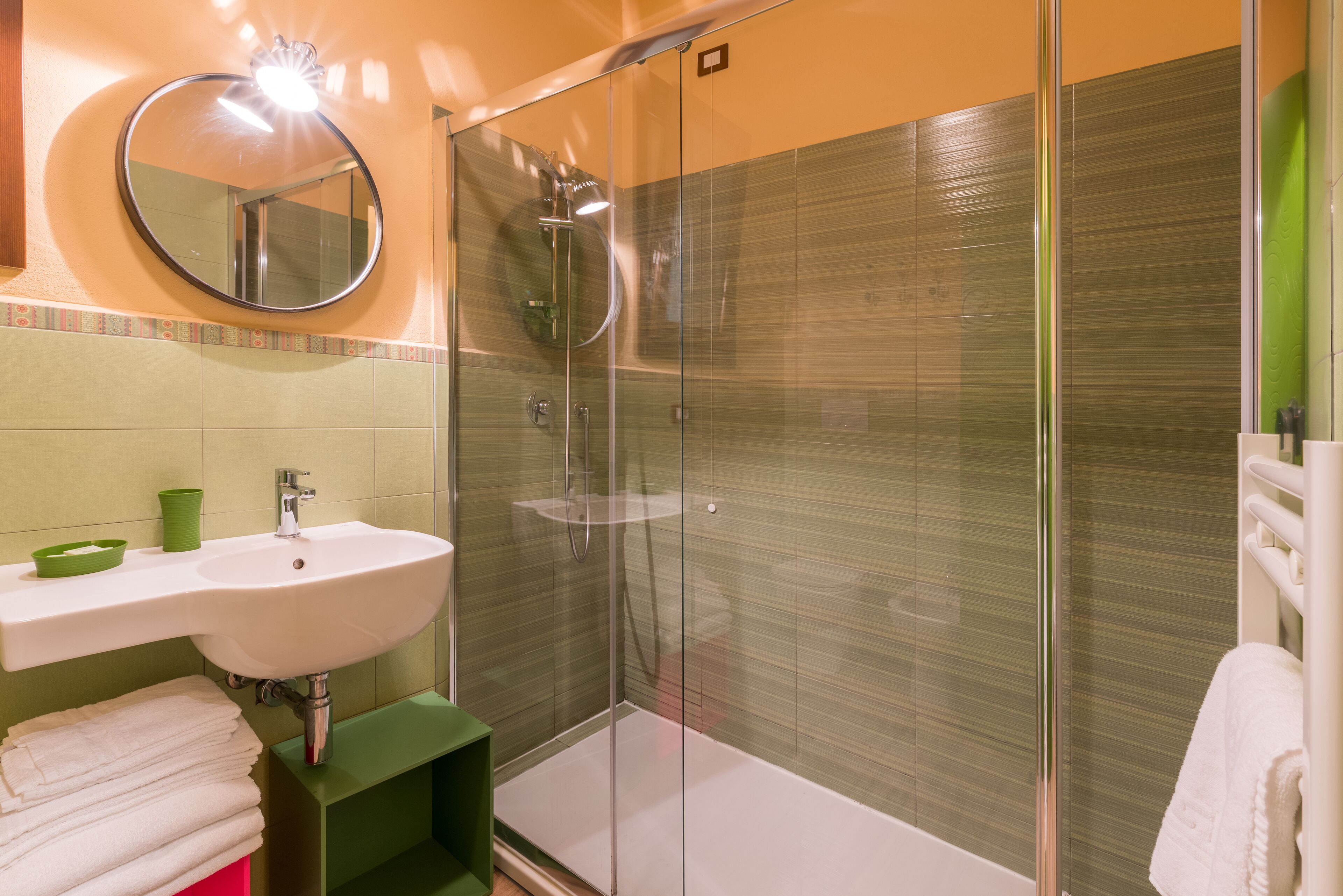 Un baño moderno con ducha de vidrio, lavamanos blanco y mueble de tocador verde.