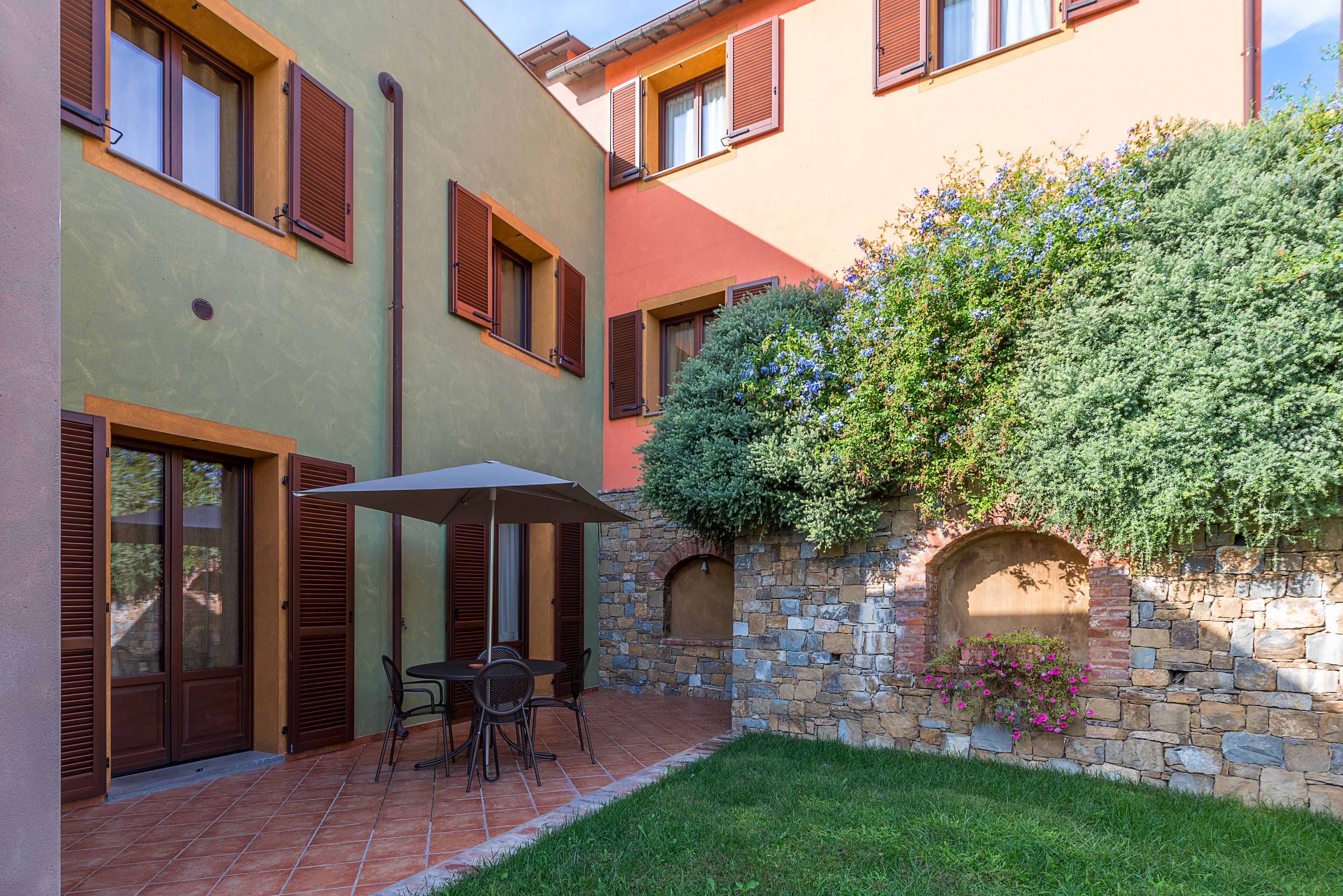 Un patio con una mesa y sillas, un muro de piedra con una jardinera, y un pequeño arco.