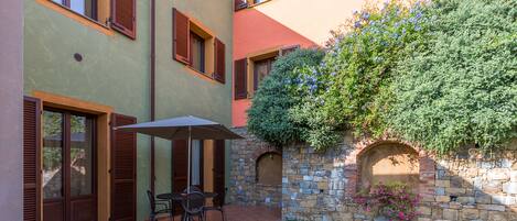 A patio with a table and chairs, a stone wall with a flower box, and a small archway.