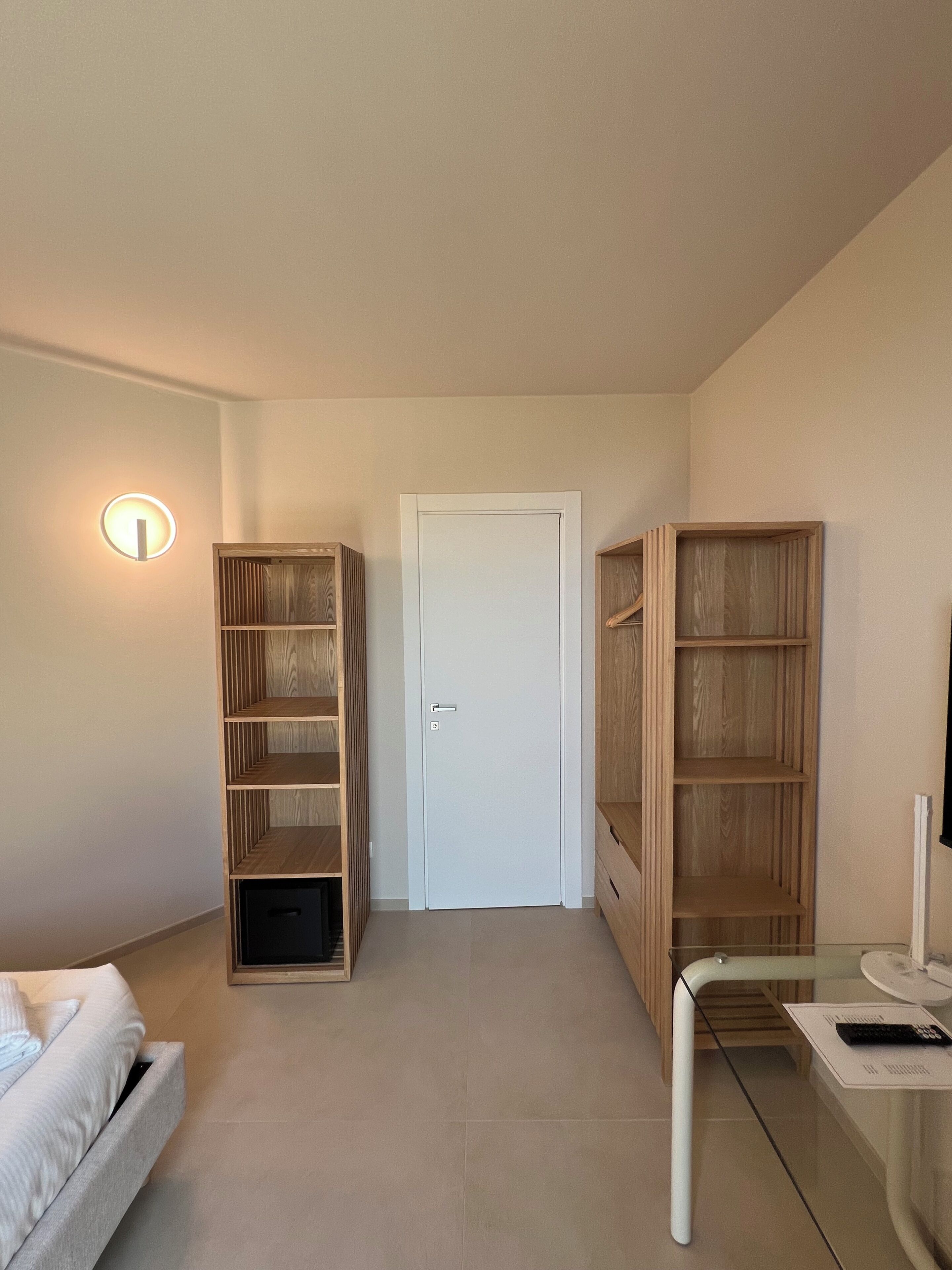A hallway with a white door, wooden shelving units, a glass table with a remote, and a white sofa.