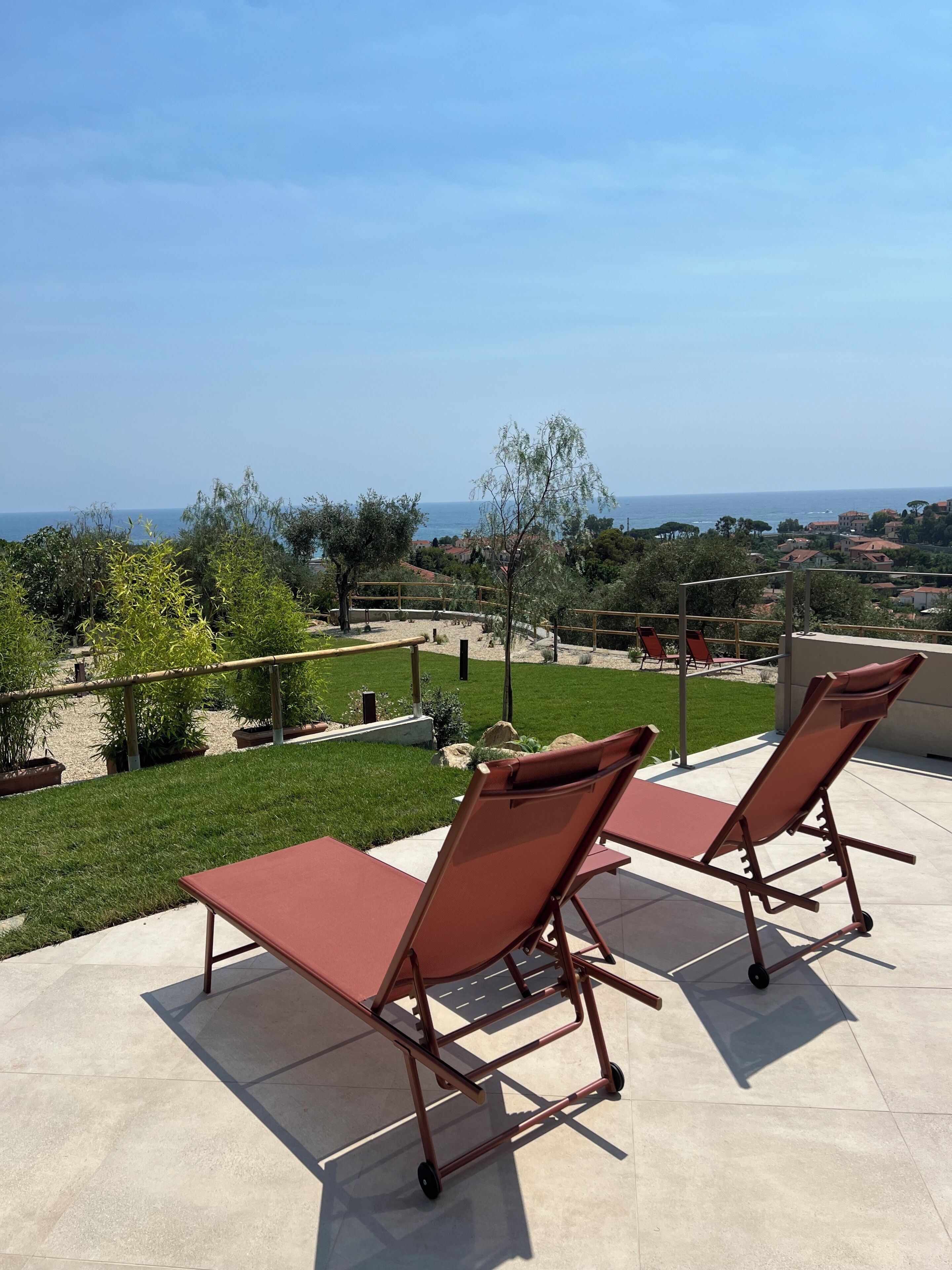 A terrace with two sun loungers, a view of the sea, and a well-maintained lawn.