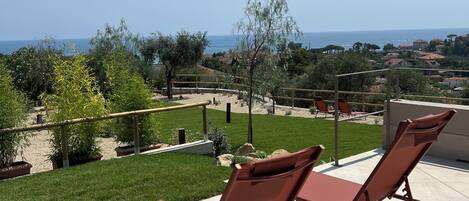 Une terrasse avec deux chaises longues, une vue sur la mer et une pelouse bien entretenue.