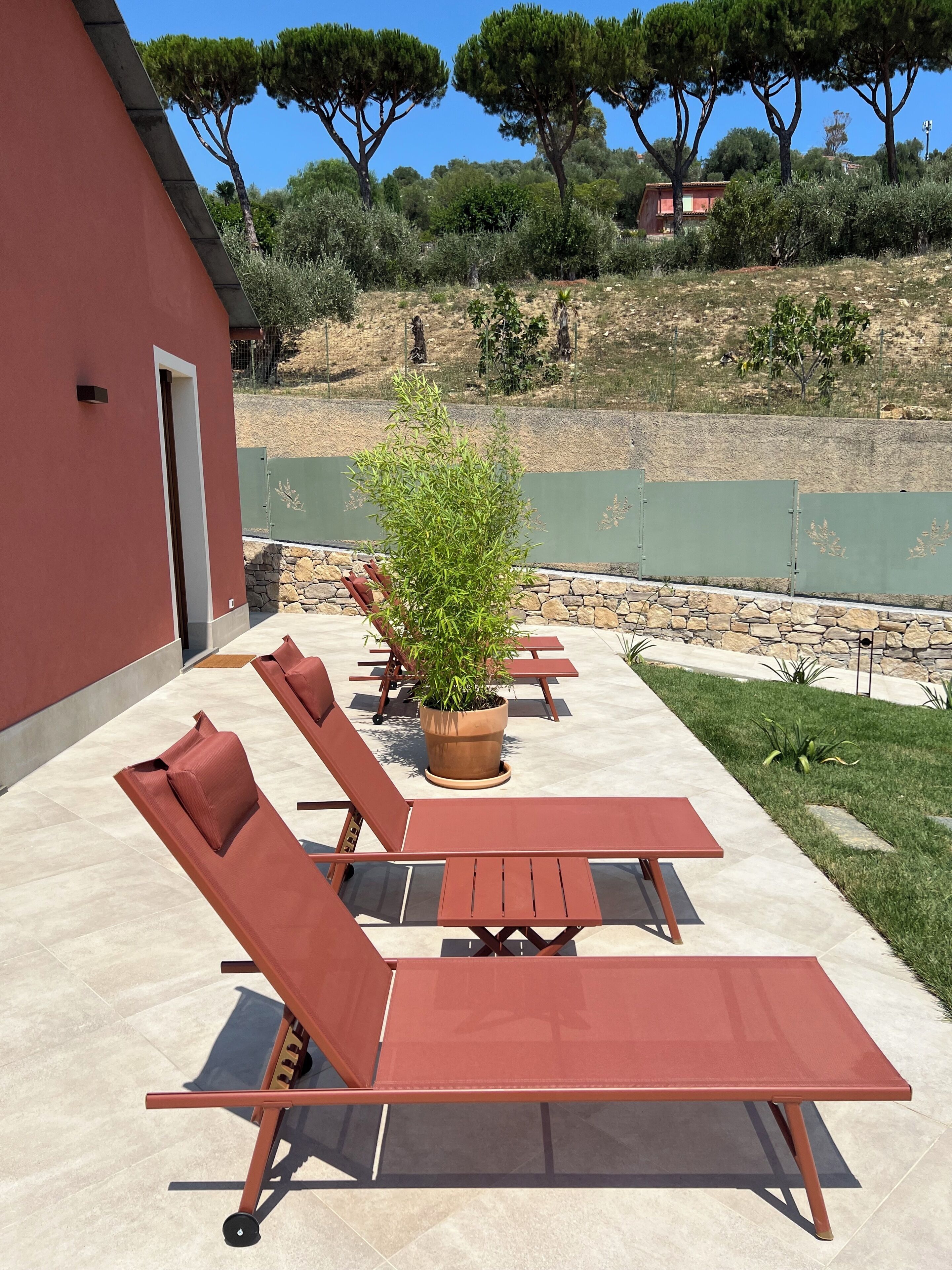A patio with sun loungers, a potted plant, and a stone wall.