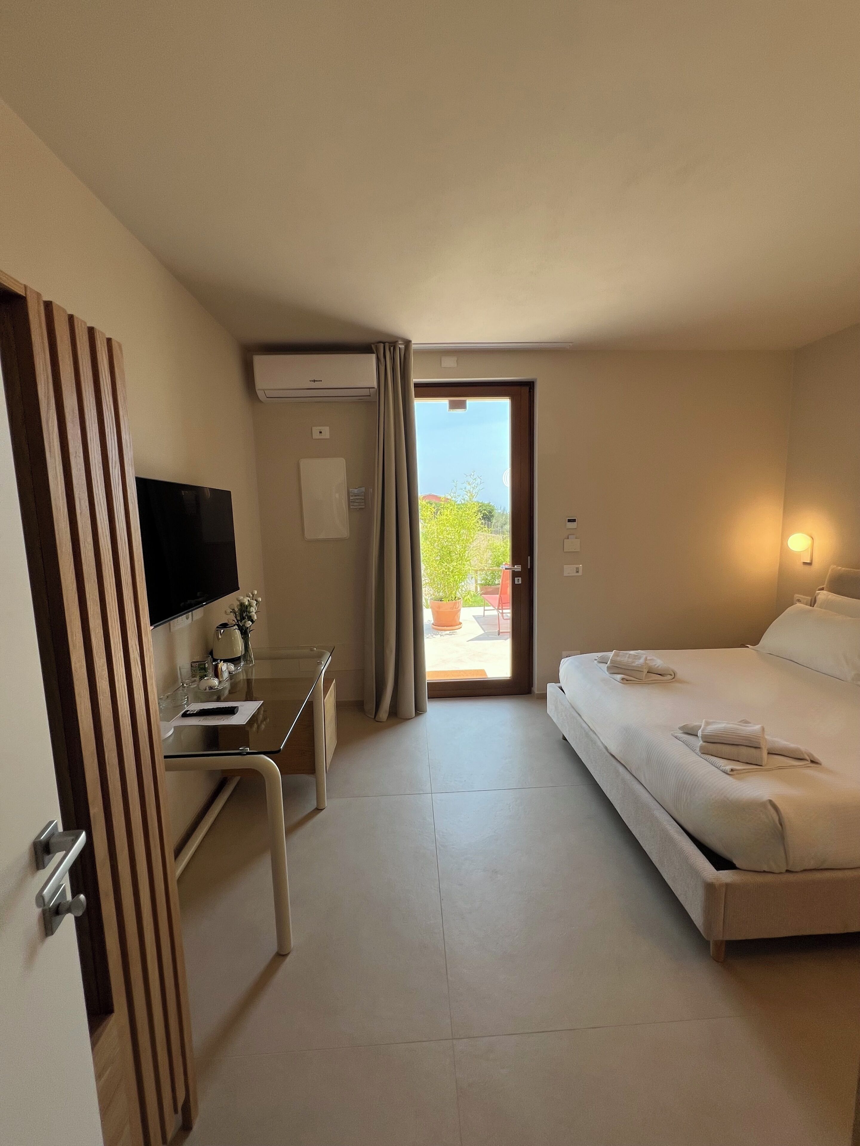 Une chambre d’hôtel équipée d’un lit, d’un bureau, d’une télévision et d’une porte coulissante donnant sur un espace extérieur.