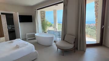 Et moderne hotelværelse med seng, badekar, stol og balkon med havudsigt.