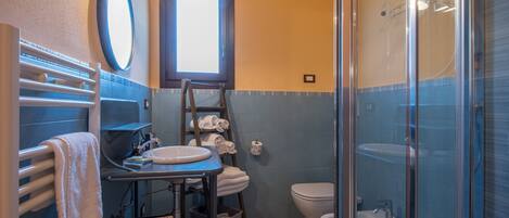 A bathroom with a shower, a sink, a toilet, a towel rack, and a window.