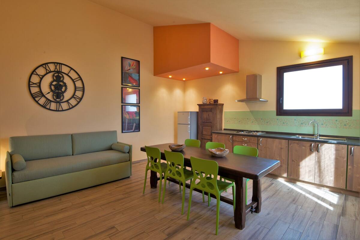 Una cocina moderna con comedor, que presenta una mesa de madera, sillas verdes y un sofá verde.